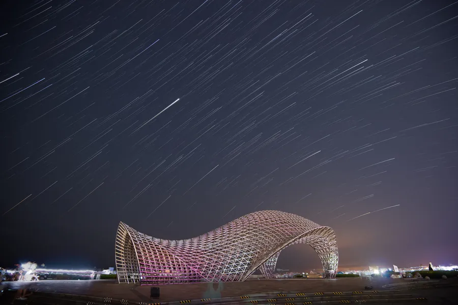 Star trails arcing over a lattice wave pavilion at night