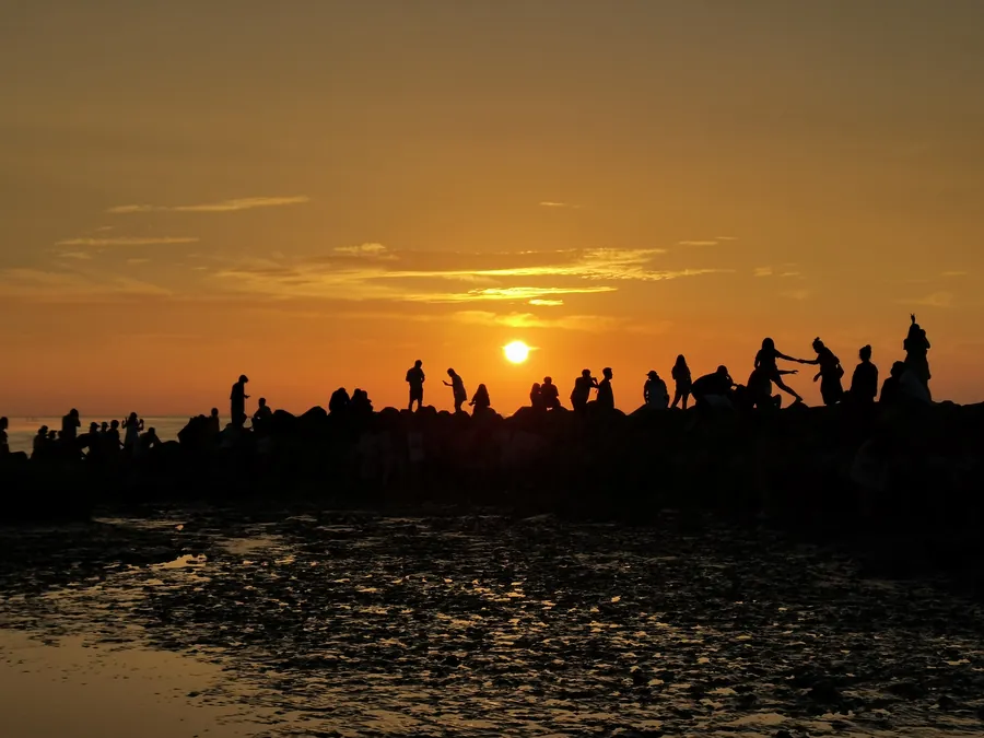 Silhouettes on seaside rocks at sunset, wet tidal flats in front