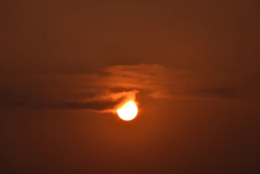 An orange sun partly veiled by wisps of cloud